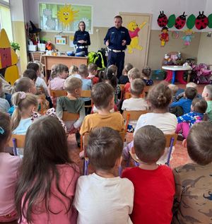 Policjant i policjantka stoją na środku sali, w której przed nimi siedzi duża grupa dzieci.