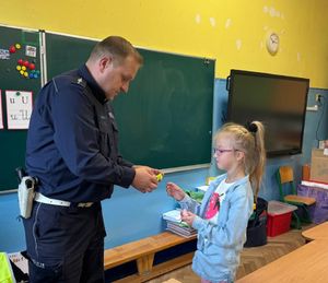 Policjant przekazuje uczniom element odblaskowy.