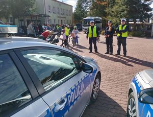 Trzech policjantów stoi przed radiowozem, obok nich osoby na rowerach.