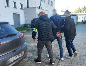 Dwóch policjantów prowadzi w środku zatrzymanego mężczyznę.