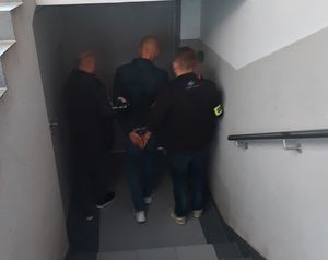 Dwóch policjantów stoi przy drzwiach z zatrzymanym mężczyzną.