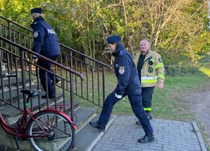 Policjantki i strażak wchodzą do budynku przedszkola, idą z wyprowadzanymi dziećmi.