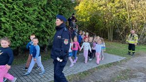 Policjantki i strażak wchodzą do budynku przedszkola, idą z wyprowadzanymi dziećmi.