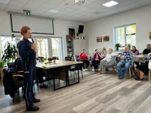 Policjantka mówi przez mikrofon do osób siedzących przed nią na sali.