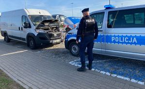 Policjant stoi przy radiowozie a przed nim stoi biały bus.