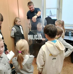 Policjant pokazuje grupie dzieci tarczę z napisem policja.