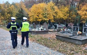 Dwóch policjantów idzie alejkami cmentarnymi.