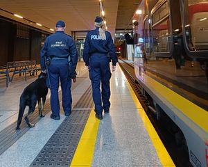 Policjantka i funkcjonariusz kolei trzyma psa, oboje chodzą po dworcu kolejowym.