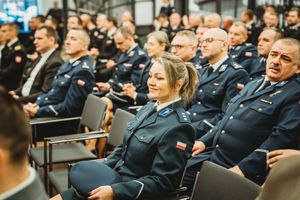 Policjantka siedzi na krześle, wśród innych policjantów.