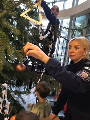 Policjanci z dziećmi dekorują choinkę.