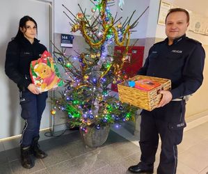 policjantka i policjant stoją przy choince i trzymają prezenty.