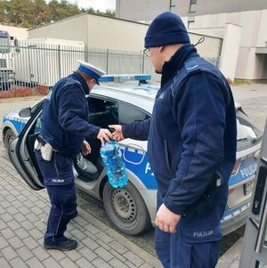 Dwóch policjantów pakuje do radiowozu baniaki z wodą.