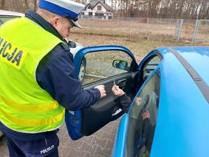 Policjant stoi przy samochodzie i przekazuje pachnącą zawieszkę.