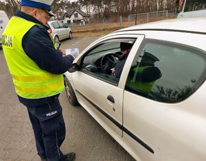 Policjant stoi przy samochodzie i przekazuje pachnącą zawieszkę.