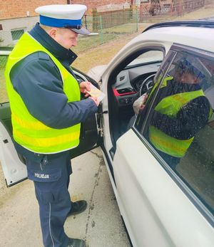 Policjant stoi przy samochodzie i przekazuje pachnącą zawieszkę.