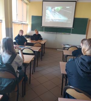 Dwie policjantki siedzą przed grupą młodzieży siedzącej w ławkach.