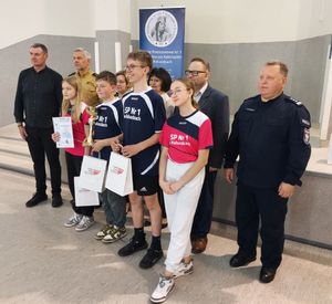 Policjant, strażak i nauczyciele stoją przy grupie młodych osób.