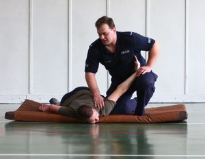 Policjant prezentuje chwyty obezwładniające na leżącym na materacu mężczyźnie.