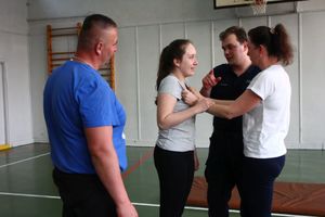 Dwie kobiety uczą się chwytów obezwładniających obok nich stoją policjanci.