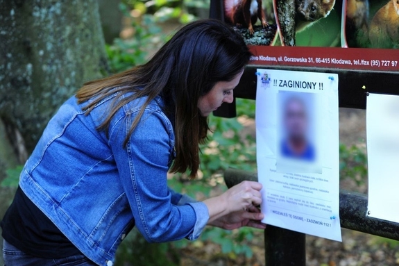 Kobieta wiesza informację o zaginionej osobie.