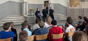 Policjanci stoją na środku sali w której siedzą przed nimi uczniowie.