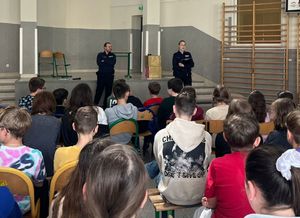 Policjanci stoją na środku sali w której siedzą przed nimi uczniowie.