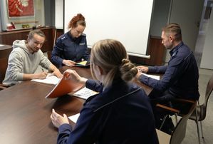 Policjanci i pracownik starostwa siedzą przy stole i oceniają prace plastyczne.