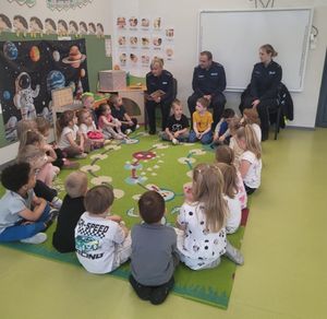 Policjanci siedzą przed grupą przedszkolaków i czytają książkę.