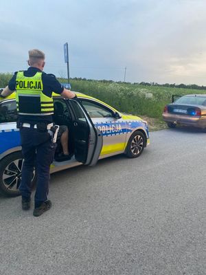 Policjant stoi przy radiowozie, w którym siedzi zatrzymany mężczyzna.