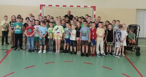 Policjant stoi na hali sportowej z grupą dzieci.