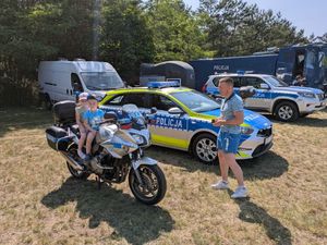 Zainteresowani stoją przy radiowozach policyjnych i motocyklach.
