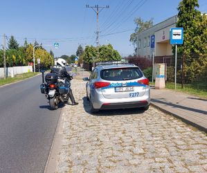 Policjant jedzie motocyklem, obok stoi radiowóz.