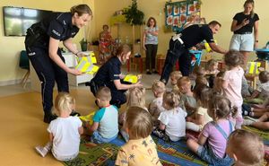 policjanci rozdają kamizelki odblaskowe dzieciom.