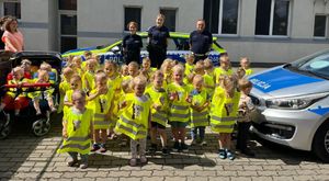 Policjanci stoją w grupie dzieci z kamizelkami odblaskowymi.