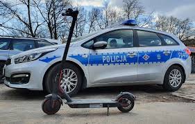 Hulajnoga elektryczna na tle radiowozu.