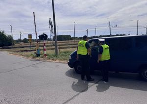 Policjant i strażnik ochrony kolei kontrolują samochody.