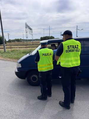Policjant i strażnik ochrony kolei kontrolują samochody.