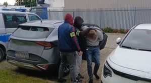 Dwóch policjantów prowadzi zatrzymanego mężczyznę.