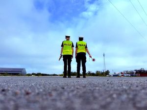 Dwie policjantki stoją na drodze, jedna trzyma urządzenie do pomiaru trzeźwości a druga tarczę do zatrzymywania pojazdów.