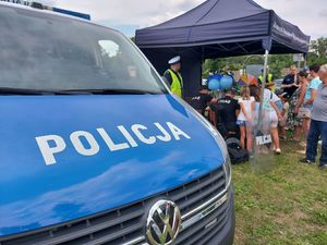 Policjanci i policjantki rozmawiają z mieszkańcami przy policyjnym stanowisku.
