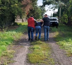 Dwóch policjantów prowadzi zatrzymanego mężczyznę.