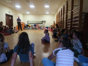 Policjant stoi na środku sali, w której siedzą dzieci.