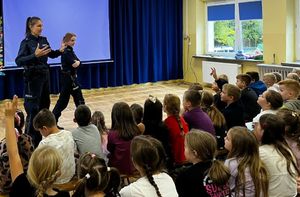 Policjantki stoją na środku sali, przed nimi siedzą dzieci.