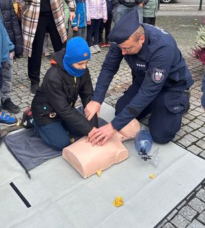Policjanci prowadzą pokaz akcji resuscytacyjnej, obok nich są dzieci.