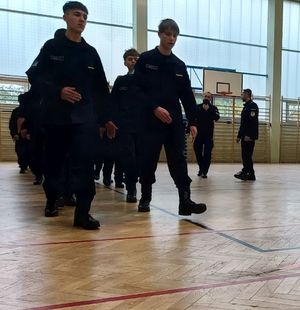 Dwóch policjantów szkoli uczniów klas mundurowych z musztry policyjnej.