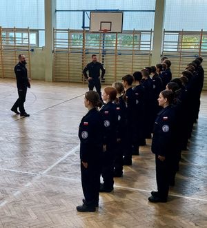 Dwóch policjantów szkoli uczniów klas mundurowych z musztry policyjnej.