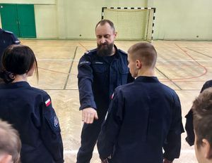 Dwóch policjantów szkoli uczniów klas mundurowych z musztry policyjnej.
