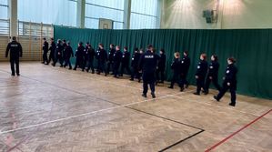 Dwóch policjantów szkoli uczniów klas mundurowych z musztry policyjnej.