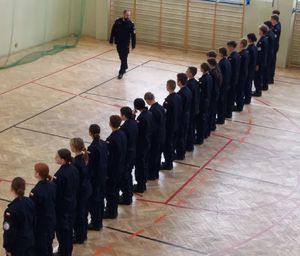 Dwóch policjantów szkoli uczniów klas mundurowych z musztry policyjnej.