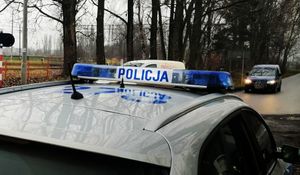 Zaparkowany radiowóz przy drodze, którą jadą samochody.